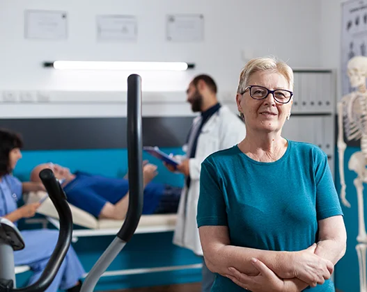 Senior woman smiling, with a posture specialist consulting a patient in the background